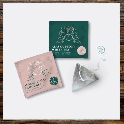 Tea packages and a triangle tea bag on a white surface with a wooden border | Alaska Beauty Peony Cooperative | Homer, AK